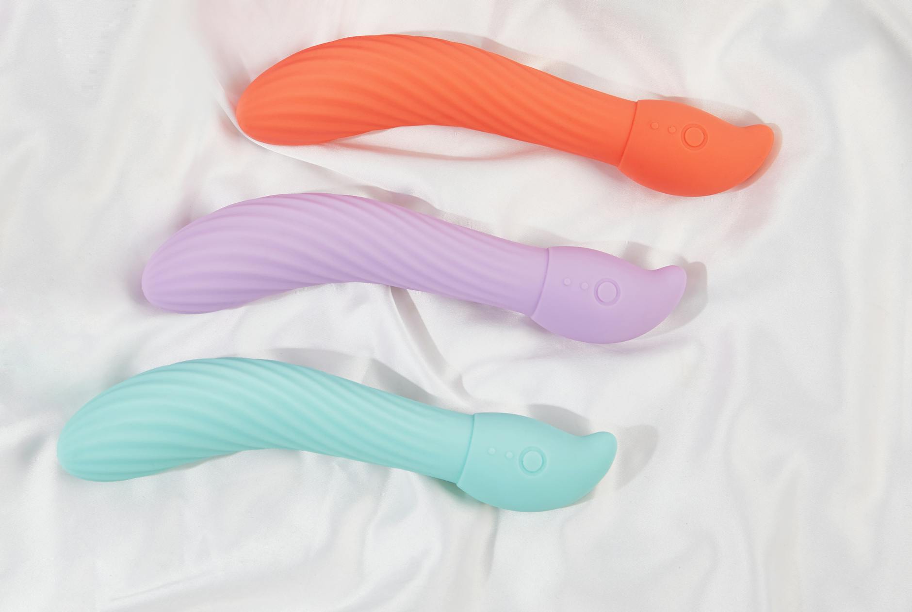 Three colorful vibrators arranged on white fabric, highlighting smooth texture and design detail.