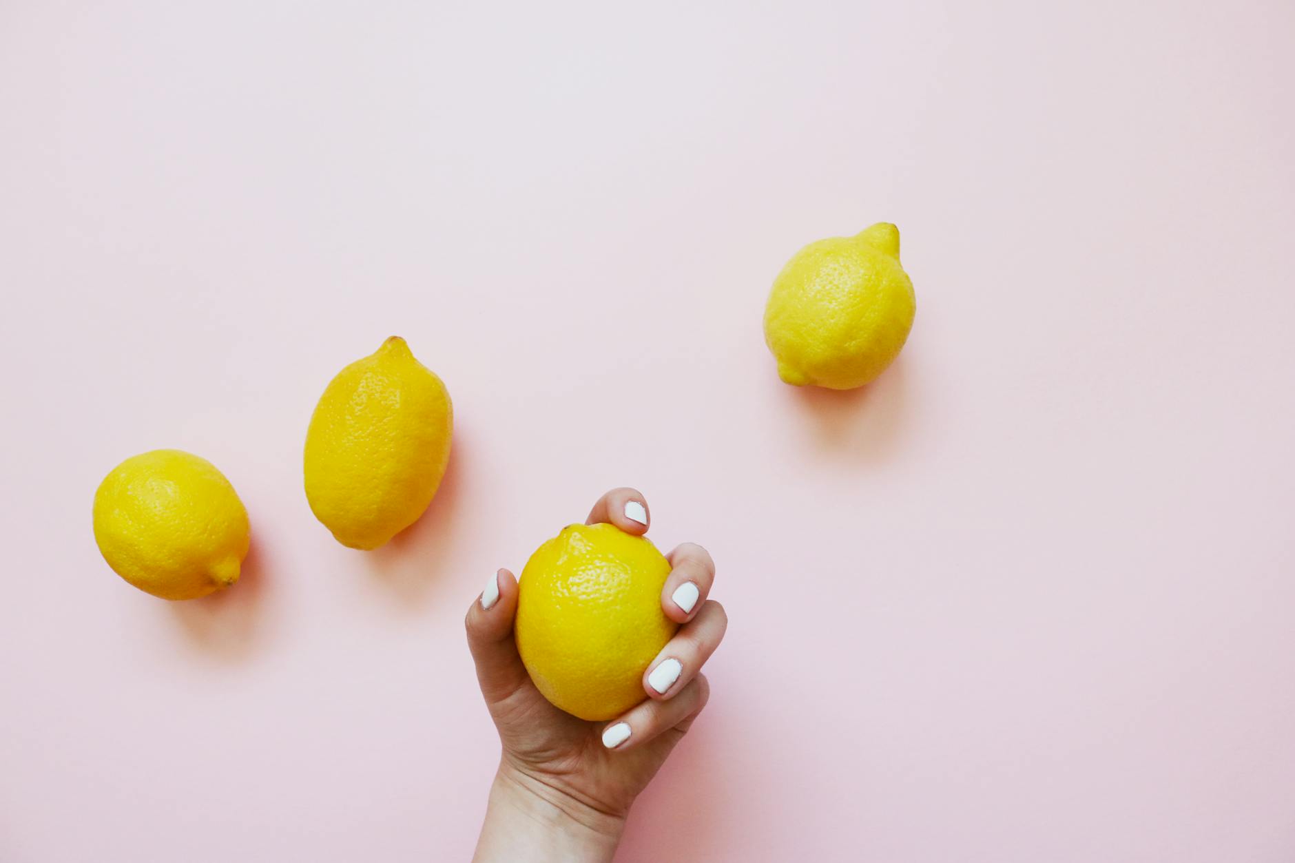 A hand holding a fresh lemon on a soft pink background, symbolizing the natural approach to pleasure and sensitivity.