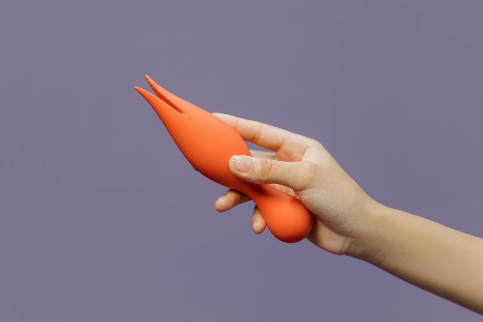 A hand holding a lemon vibrator against a minimalist purple backdrop, showing modern sensual design