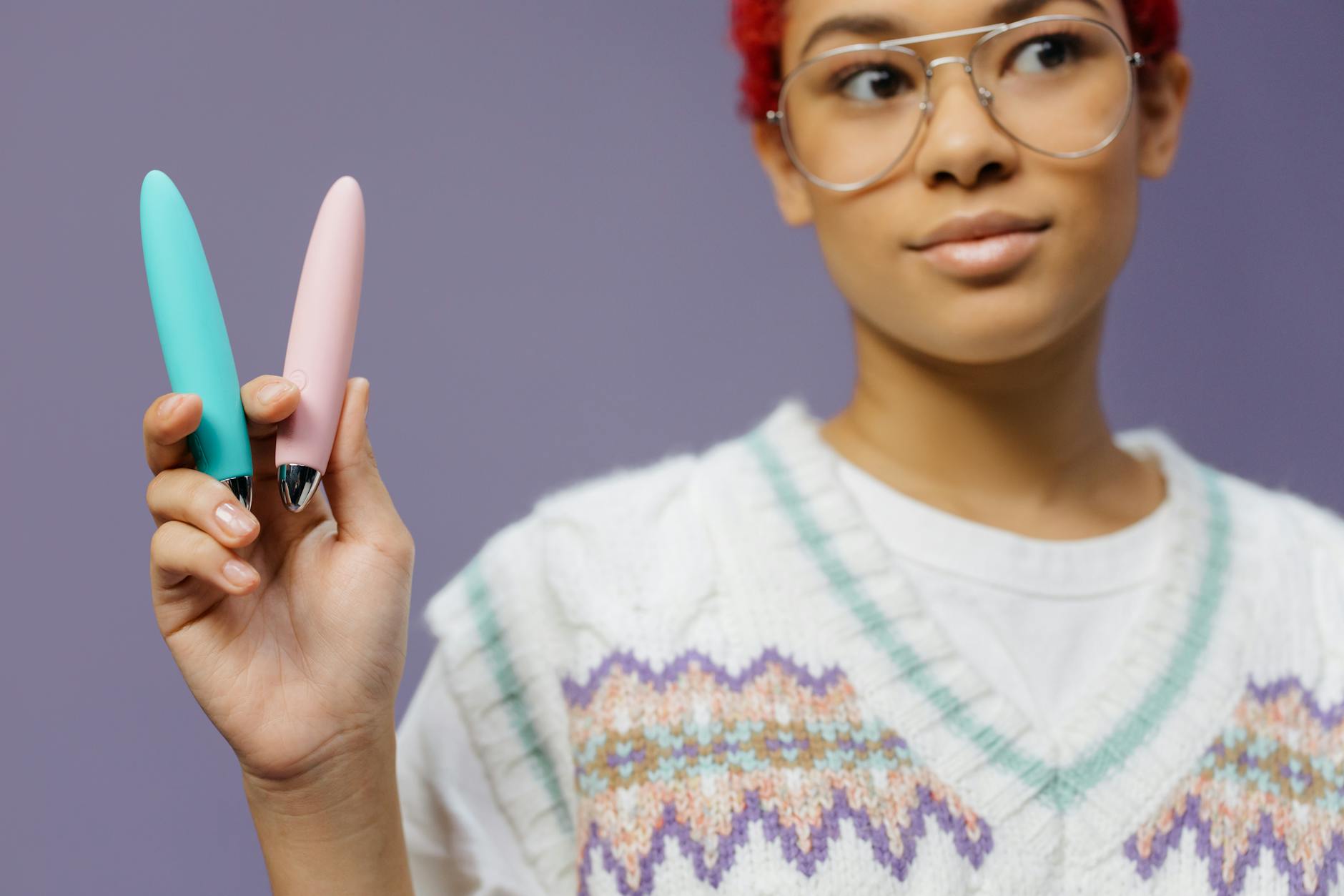 Woman holding colorful vibrators against a purple background, representing sexual wellness options