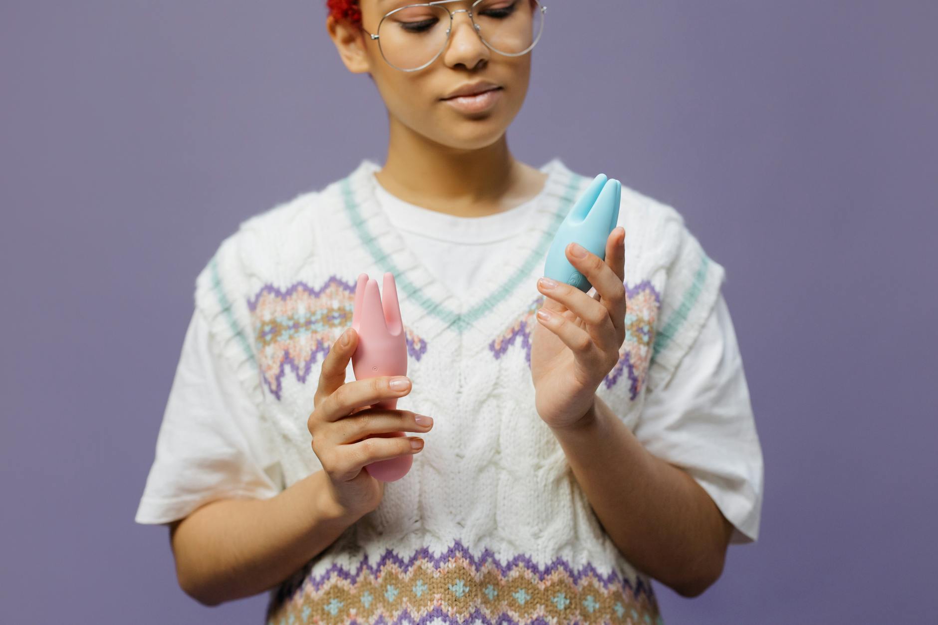 Woman holding blue and pink silicone vibrators thoughtfully in candlelit setting