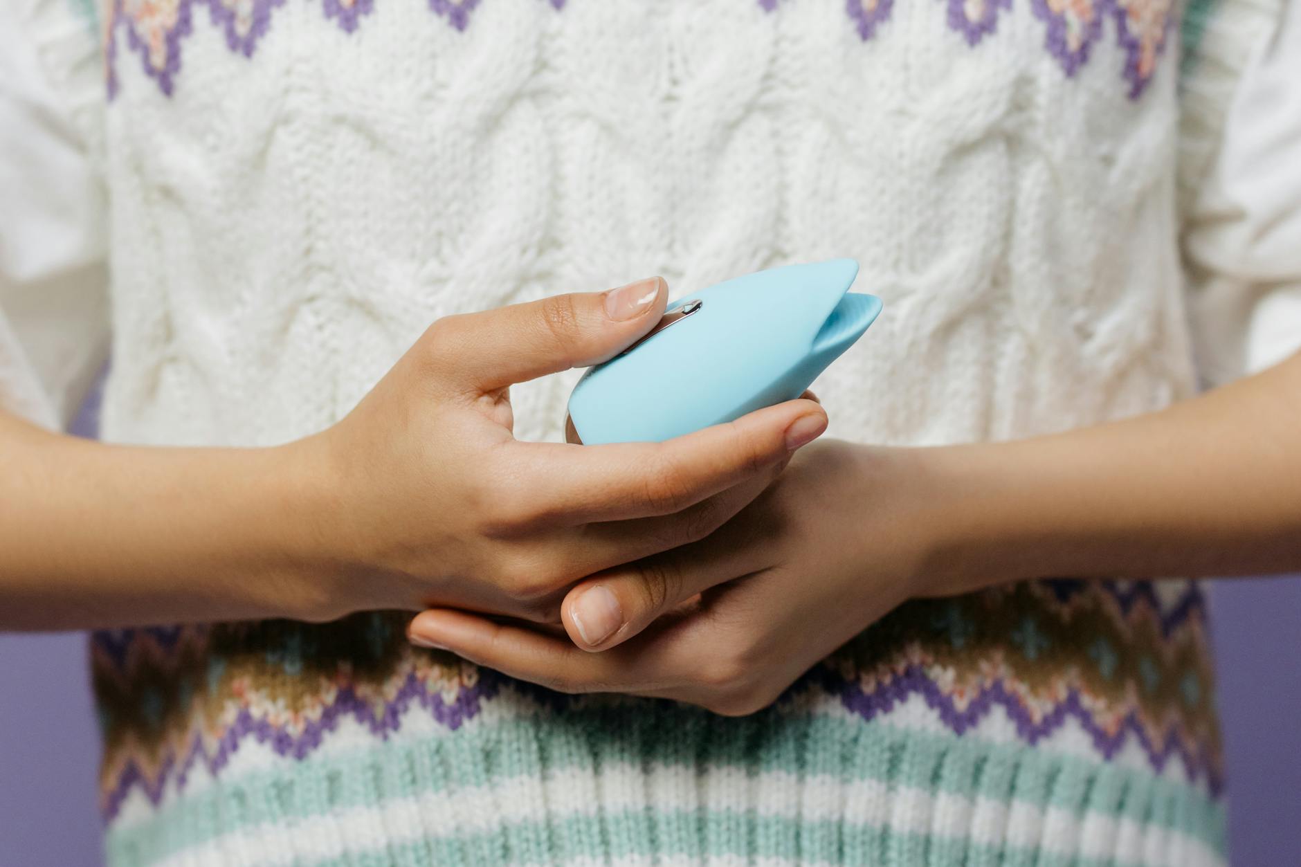 Close-up of hands holding a Lem clitoral vibrator against a textured sweater