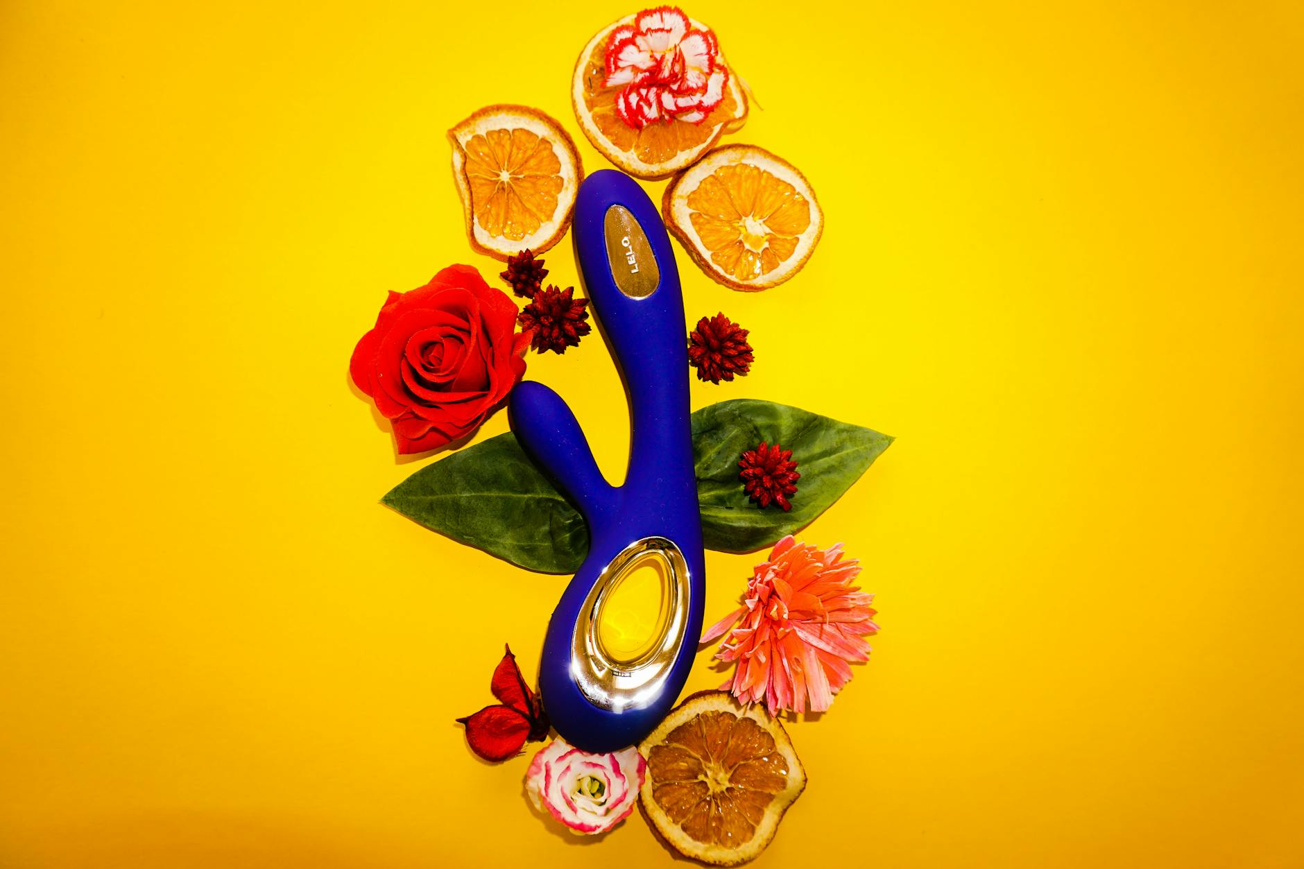 Minimalist arrangement of a blue vibrator and fresh lemons on a yellow background, symbolizing pleasure and wellness