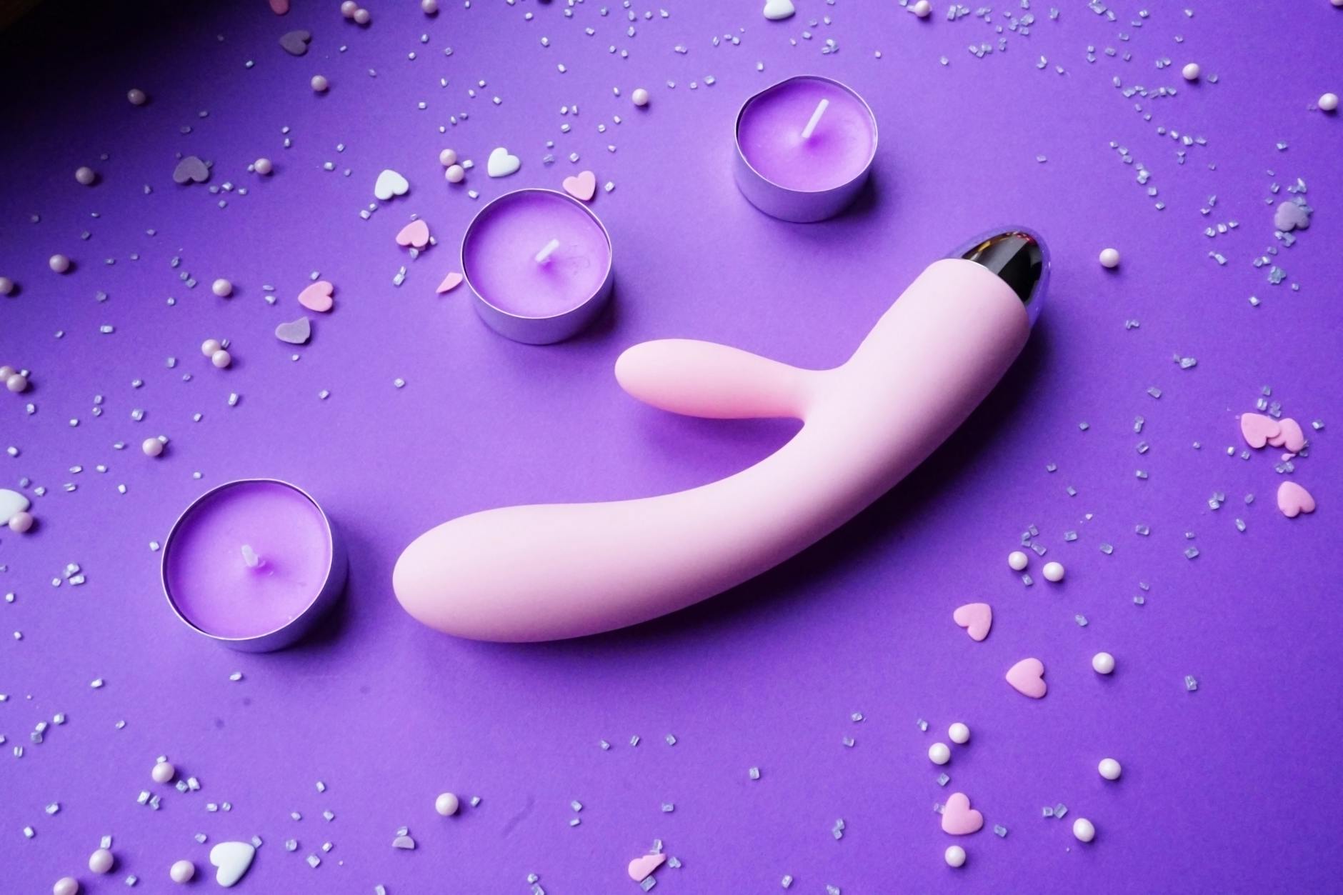 Pink vibrator on purple background with heart confetti and candles, representing intimacy and self-care during emotional recovery